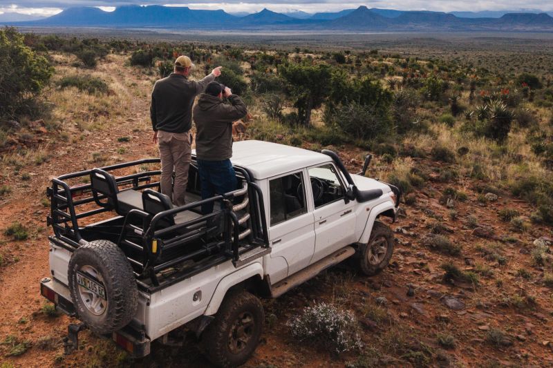 Two people safari from pickup truck overlooking desert mountains