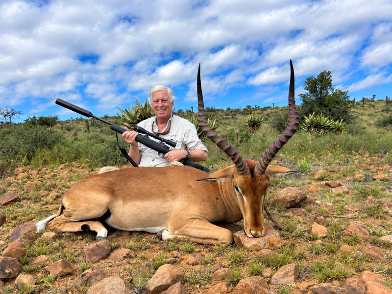 Hunter posing with rifle beside large antelope trophy
