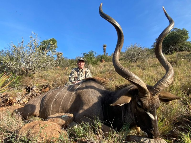 Hunter poses behind a large kudu with spiraled horns.