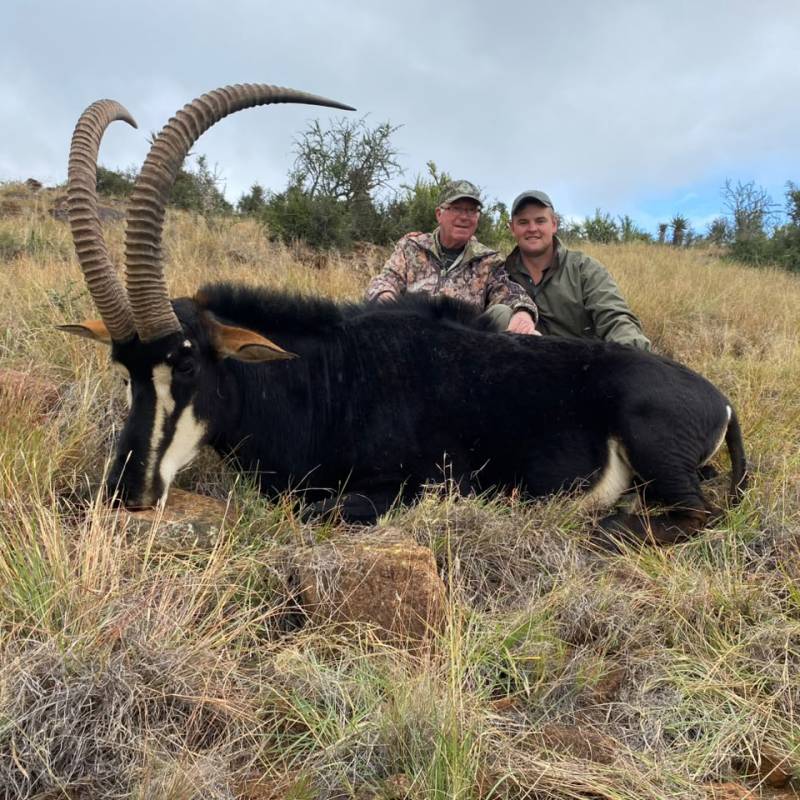 Two hunters pose behind a large sable antelope