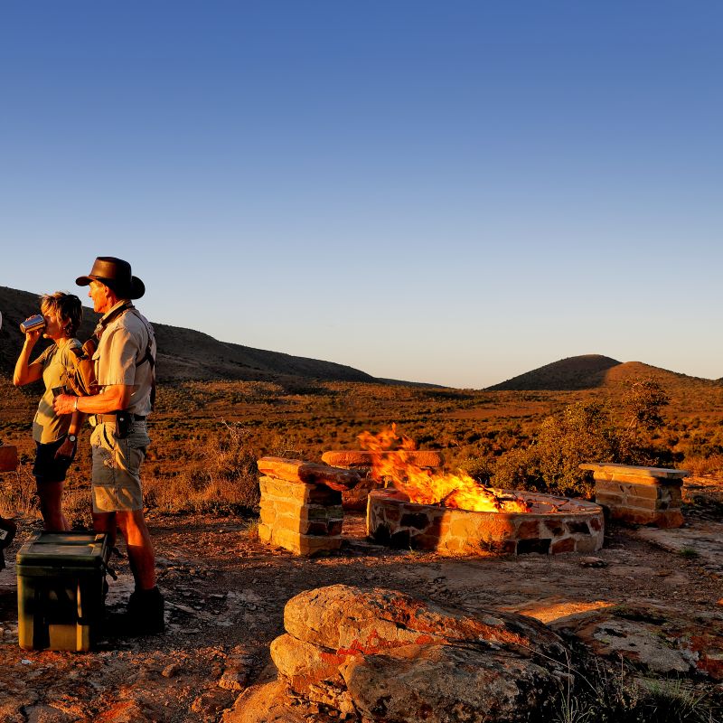 Couple beside campfire in rugged hills at sunset