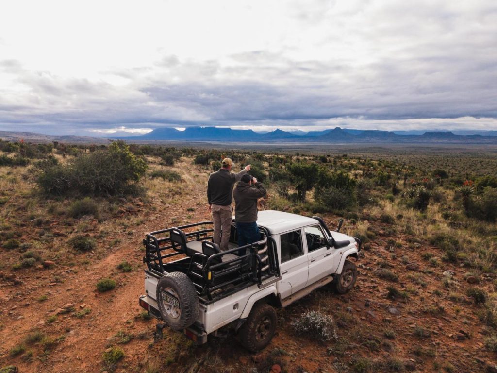 Two people viewing mountains from a white off-road truck