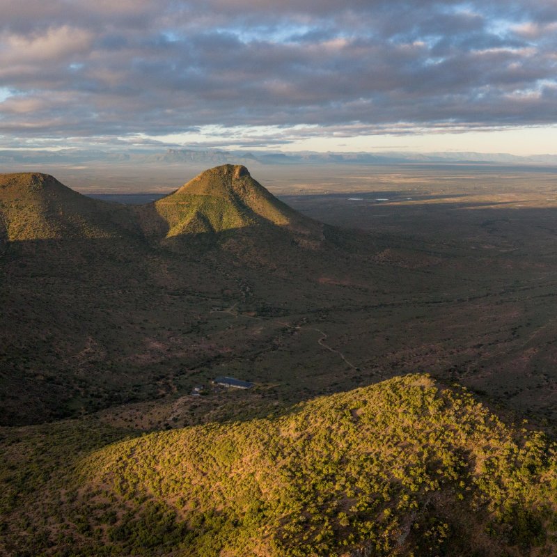 Sunlit volcanic hills overlooking a vast plain beneath cloudy skies