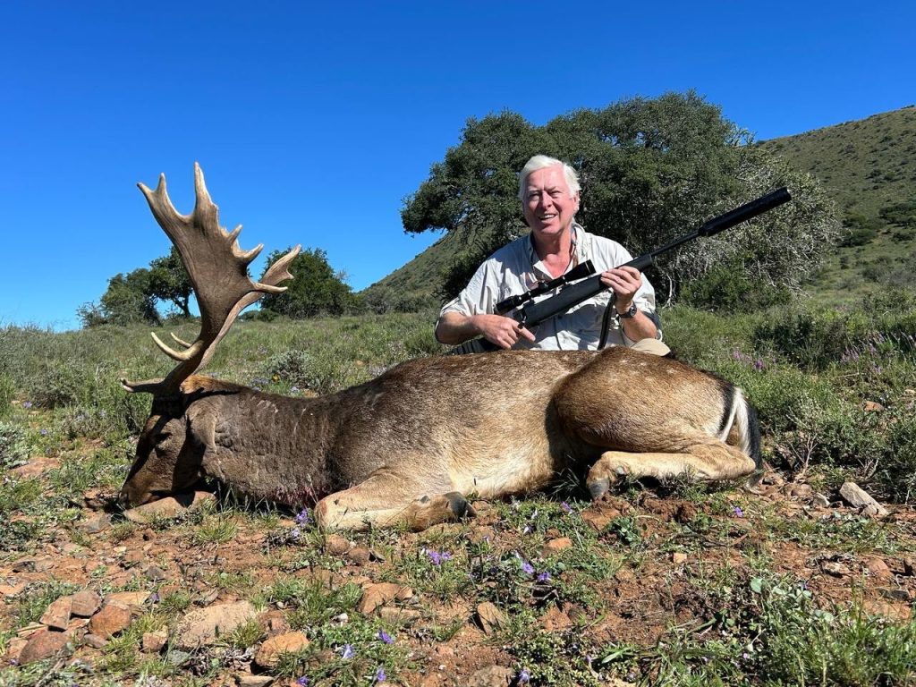 Hunter posing with rifle beside a large deer